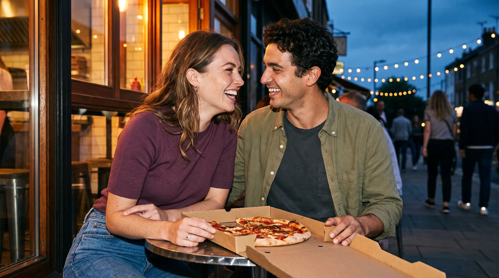 A couple laughing over pizza on a casual evening date